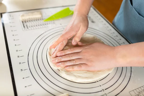 Close-up on female hands crumpling fresh kneaded dough on a kitchen baking mat.