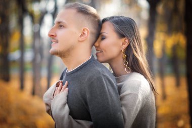 Genç bir kadın erkeğine arkadan sarılıyor, erkek uzaklığa bakıyor..