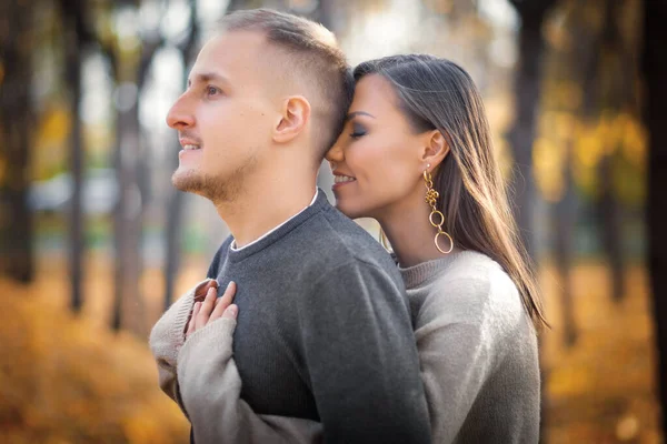 Genç bir kadın erkeğine arkadan sarılıyor, erkek uzaklığa bakıyor..