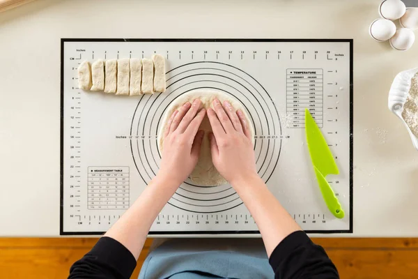 Flat lay of cook hands kneading rolled out dough on a silicone baking mat with round markings of different diameters.