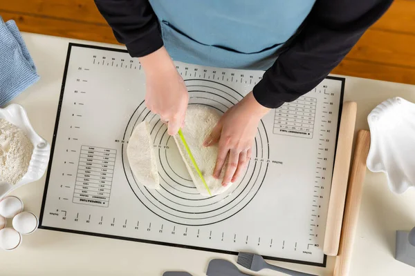 Cutting dough on a kithen silicone baking mat with a special plastic knife, flat lay.