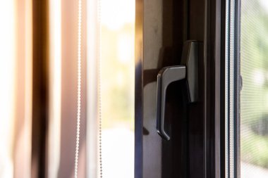 Window handle on a brown metal-plastic window through which the sun shines.