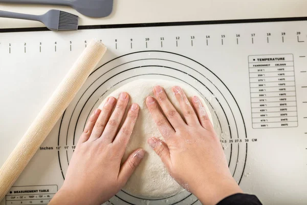 Kneading the dough on a silicone baking mat with round markings of different diameters to obtain a round shape, top view.