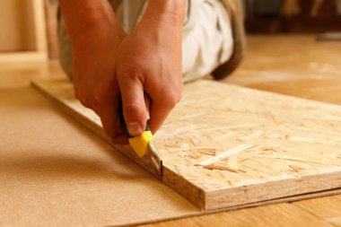 Close-up on the hands of a Carpenter who cuts fiberboard with a mounting knife using OSB.