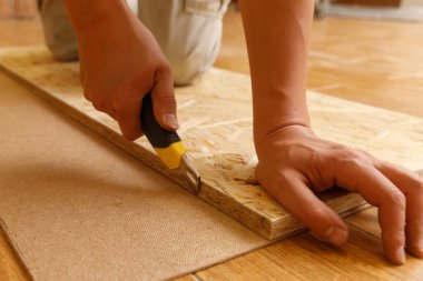 Carpenter cuts fiberboard with a mounting knife using OSB.