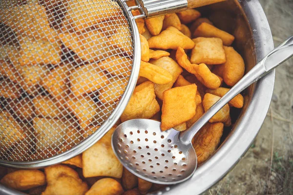Traditional Kazakh and central asian fresh baursaks in a large dish with a colander and slotted spoon.