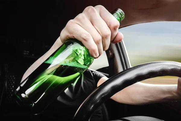 Close-up of a bottle of beer in the drivers hand at the wheel. Alcohol driving concept.