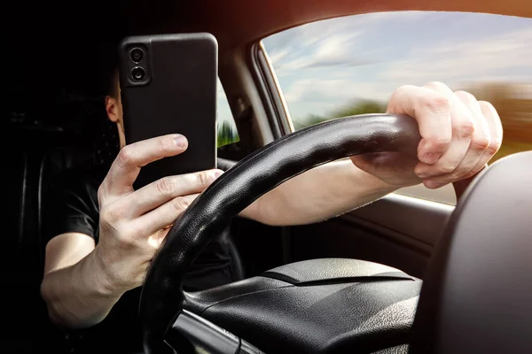 The driver at the wheel of a car uses a smartphone, distracted from the road.