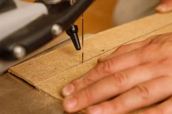 Close-up on the process of sawing wood board on a scroll saw in carpenter workshop.