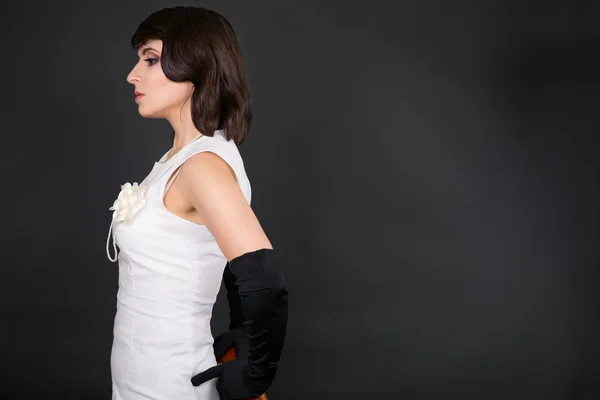 Mädchen mit Make-up in einem weißen Kleid und schwarzen Handschuhen auf schwarzem Hintergrund — Stockfoto