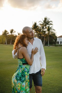 Dominik Cumhuriyeti 'ndeki tropikal bir adada golf kulübünde yürüyüş yapan güzel bir çift öpüşüyor ve sarılıyor.
