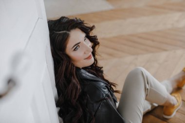 Güzel kıvırcık saçlı, deri ceketli esmer bir kız lüks saçlar için poz veriyor.