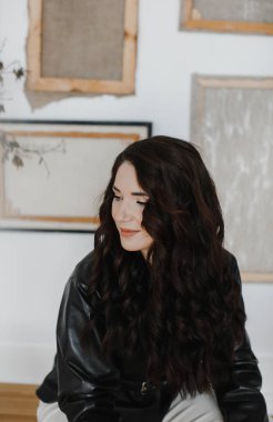 Güzel kıvırcık saçlı, deri ceketli esmer bir kız lüks saçlar için poz veriyor.