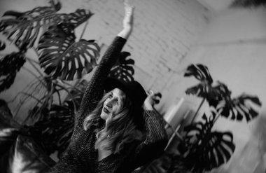 Kısa siyah elbisesi, şapkası ve ayakkabıları olan güzel, seksi, duygusal bir kız bir partide şık bir stüdyoda poz veriyor.