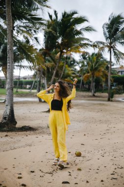 Sarı takım elbiseli güzel, sıska bir esmer kız Dominik Cumhuriyeti 'ndeki bir golf kulübünde tropik palmiye ağaçlarının yanında poz veriyor.