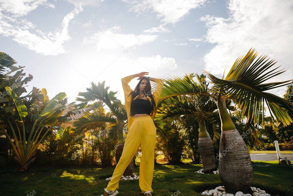 a beautiful skinny brunette girl in a yellow suit poses on vacation near tropical palm trees at a golf club in the Dominican Republic