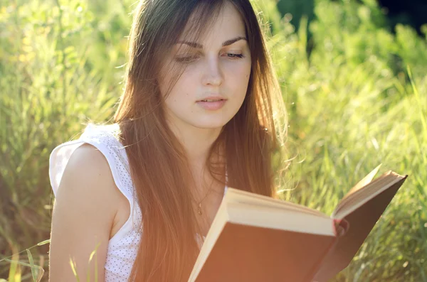 Vacker flicka läsa en bok på en äng — Stockfoto