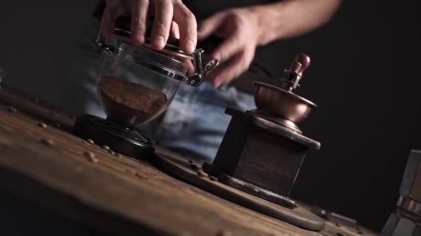 Измельчение ароматных кофейных зерен с ручной кофемолкой на деревянном столе на темном фоне — стоковое видео