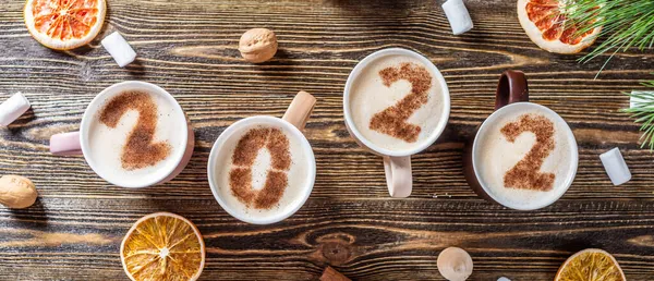Yeni yıl ve Noel için 2022 numaralı kart. Tahta arka planda süt köpüğü figürlü bir fincan kahve. Yukarıdan manzara. Düz yatıyordu
