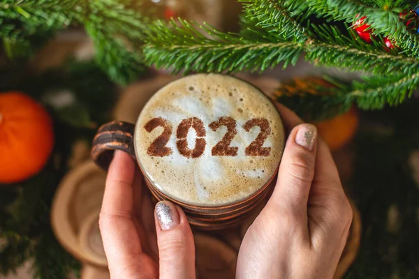 クリスマスツリーの緑の枝を持つ木製の背景に番号2022とカプチーノコーヒーのマグカップ クリスマスの朝の熱い飲み物から暖かく居心地の良い — ストック写真