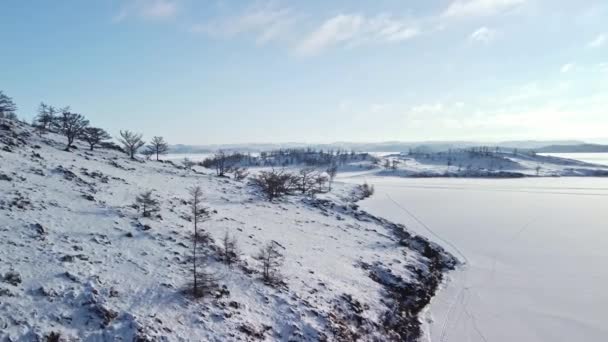 Paisaje invernal del lago Baikal cubierto de nieve con rocas y colinas en un día soleado y helado. Disparando desde un dron — Vídeo de stock