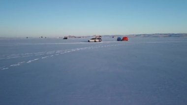 Karla kaplı Baykal gölünde kayaların ve tepelerin arka planında kış balıkçılığı. Soğuk, güneşli bir gün.