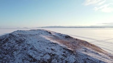 Güneşli bir günde, karla kaplı Baykal Gölü 'nün, kayalar ve tepelerle kaplı kış manzarası. Bir İHA 'dan ateş etmek