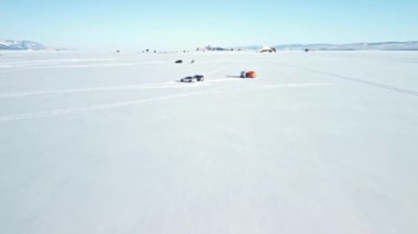 Karla kaplı Baykal gölünde kayaların ve tepelerin arka planında kış balıkçılığı. Soğuk, güneşli bir gün.