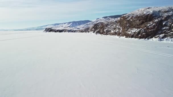 Paisagem de inverno do Lago Baikal coberto de neve com rochas e colinas em um dia gelado ensolarado. Tiroteio de um drone — Vídeo de Stock
