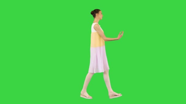 Νεαρό όμορφο κορίτσι σε λευκό-κίτρινο φόρεμα βόλτες κουνώντας το χέρι σε μια πράσινη οθόνη, Chroma Key. — Αρχείο Βίντεο