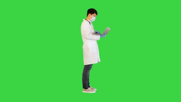 Joven médico asiático está trabajando en el ordenador portátil, buscando y escribiendo en una pantalla verde, Chroma Key. — Vídeo de stock