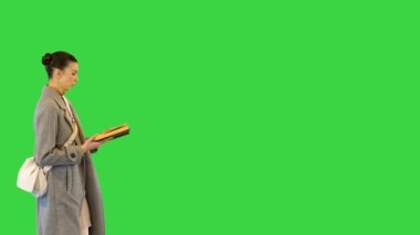 Şık giyinmiş genç bir kadın elinde bir kitapla gezer, durur ve onu yeşil ekranda kapatır, Chroma Key..