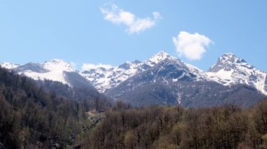 Rusya 'nın Soçi kentindeki Krasnaya Polyana' da güneşli bir günde mavi gökyüzünde beyaz bulutlu karlı dağların manzarası.