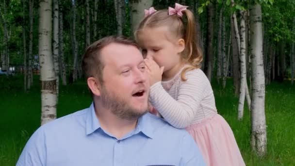 Lille datter, 3 år gammel, fortæller sin far i hendes øre og griner. Begrebet en lykkelig barndom, faderskab, forældre. Et tillidsfuldt forhold mellem forældre og børn. Fars dag – Stock-video