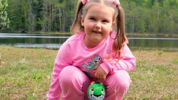 핑크 색 스웨트 셔츠를 입고 두 머리가 달린 3 살난 여자 아이가 자연스럽게 밖에서 놀고 있는 모습. 행복 한 어린 시절의 개념, 아이들의 발달 — 비디오