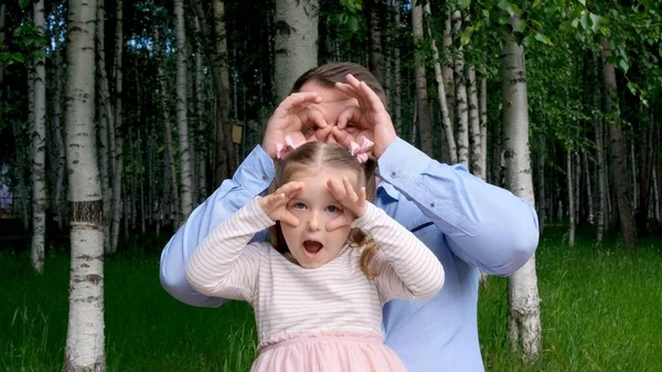 Η κορούλα 3 ετών και ο πατέρας διασκεδάζουν στο δρόμο, κάνουν γκριμάτσες, φτιάχνουν γυαλιά με τα δάχτυλά τους, σαν γυαλιά κοιτάζοντας την κάμερα με κιάλια. Καλά να περάσεις με το παιδί — Φωτογραφία Αρχείου
