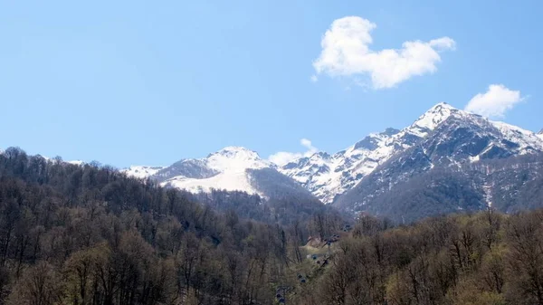 Rusya 'nın Soçi kentindeki Krasnaya Polyana' da güneşli bir günde mavi gökyüzünde beyaz bulutlar olan kar kaplı dağların güzel manzarası. Ünlü kayak merkezi. — Stok fotoğraf