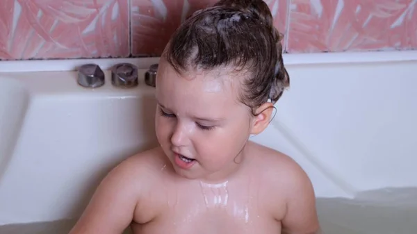 Kis vicces lány 3 éves fürdik és mossa hab a fején vízben a fürdőszobában otthon. Babaápolás, higiénia. — Stock Fotó