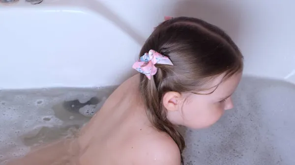 Petite fille drôle 3 ans baigne et se lave avec de la mousse sur la tête dans l'eau dans la salle de bain à la maison. Bébé concept de soins du corps, hygiène. — Photo