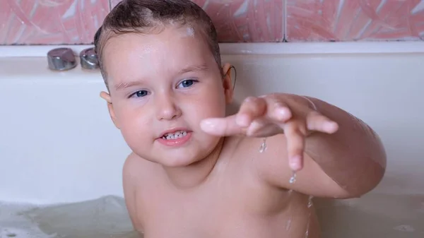 Das kleine lachende Mädchen, 3 Jahre alt, badet und wäscht sich im heimischen Badezimmer mit Schaum auf dem Kopf im Wasser. Babypflegekonzept, Hygiene. — Stockfoto