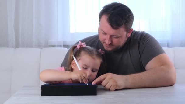 Petite fille de 3 ans dessine avec son père et regarde une leçon de dessin en ligne sur une tablette à la maison. Le concept de l'enseignement à distance école en ligne — Video