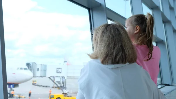Felice madre e bambina in aeroporto in previsione di atterraggio guardare fuori dalla finestra di vetro agli aerei. Il concetto di viaggi e voli sicuri. — Foto Stock