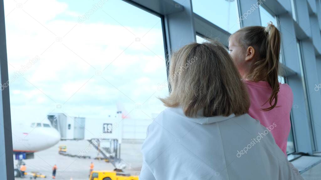 happy Mother and little girl at the airport in anticipation of landing look out the glass window at the planes. The concept of safe travel and flights.