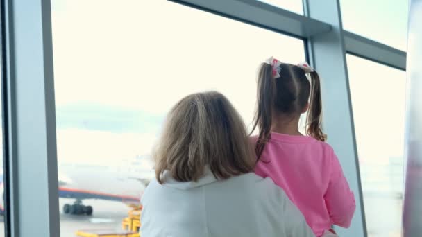 Happy Mother and little girl at the airport in anticipation of landing look out the glass window at the planes. The concept of safe travel and flights. — Stock Video