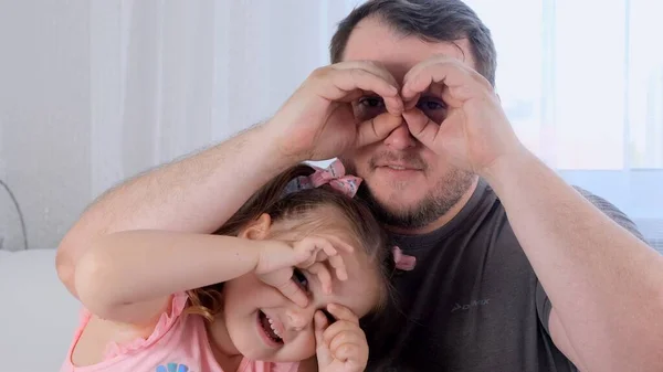 Rindo Filhinha de 3 anos e pai estão se divertindo em casa, fazendo caras engraçadas, fazendo óculos com os dedos, como óculos olhando para a câmera através de binóculos. divirta-se com criança — Fotografia de Stock