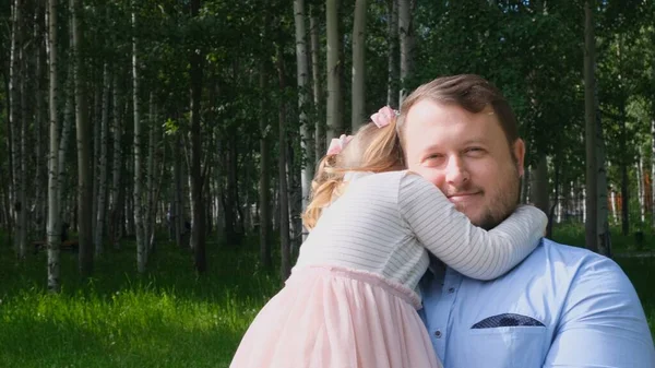 Glücklicher Vater, der seine 4-5 jährige Tochter beim Spaziergang im Park um den Hals trägt und umarmt — Stockfoto