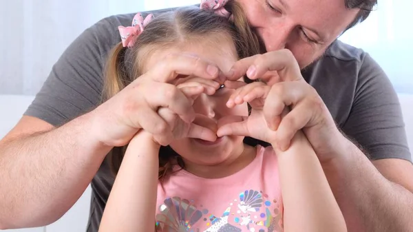 Engraçada Filhinha de 3 anos e pai estão se divertindo em casa, fazer um coração de mãos. Divirta-se com criança, tempo livre, truques, conceito tolo. dia dos pais — Fotografia de Stock