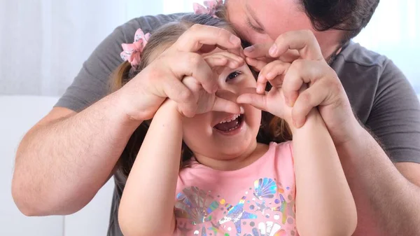 Engraçada Filhinha de 3 anos e pai estão se divertindo em casa, fazer um coração de mãos. Divirta-se com criança, tempo livre, truques, conceito tolo. dia dos pais — Fotografia de Stock