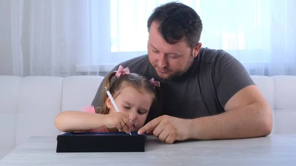 Menina de 3 anos desenha com seu pai e assiste a uma aula de desenho on-line em um tablet em casa. O conceito de ensino à distância escola on-line — Fotografia de Stock