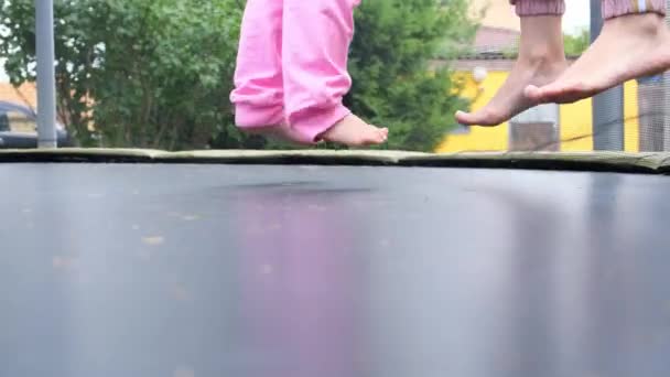 Ung kvinna och en ung flicka hoppar på en bagge, närbild. Ben flyter i luften efter att ha hoppat på en studsmatta. Familjekul, underhållning och idrott, selektivt fokus — Stockvideo